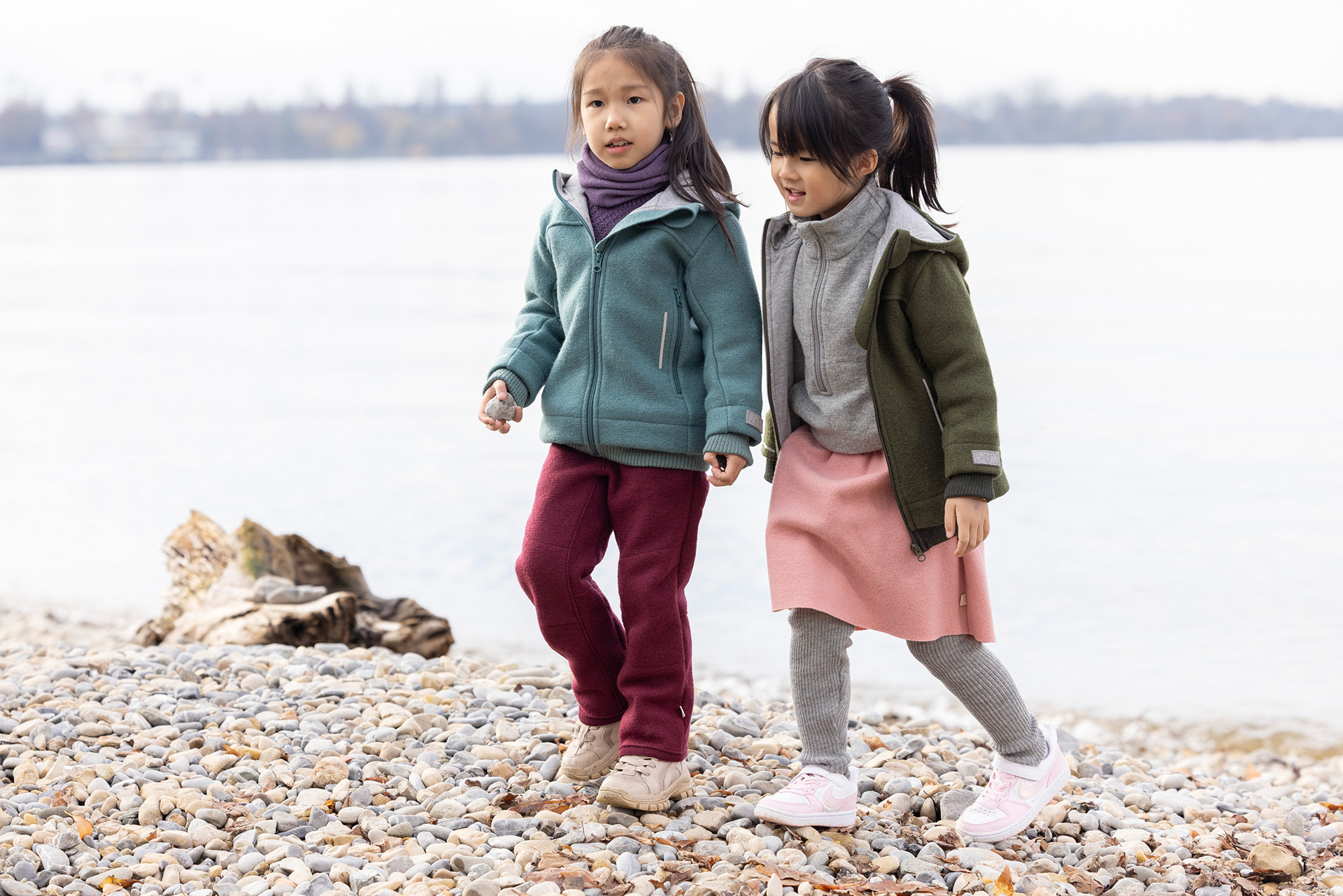 Zwei Mädchen in disana Walk-Kleidung von disana aus Bio-Merinowolle spazieren am herbstlichen Seeufer